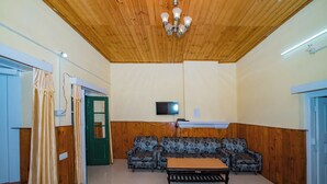 A room with a wooden ceiling, a television mounted on the wall, a sofa set, and a patterned rug. - Forest Rest House Bir (Bir)
