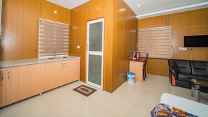 A modern kitchen with wooden cabinets, a built-in oven, and a dining area with a black sofa and a television. - Forest Rest House Bir (Bir)