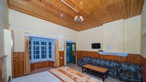A room with a bed, a sofa, a table, a wooden ceiling, and a television. - Forest Rest House Bir (Bir)