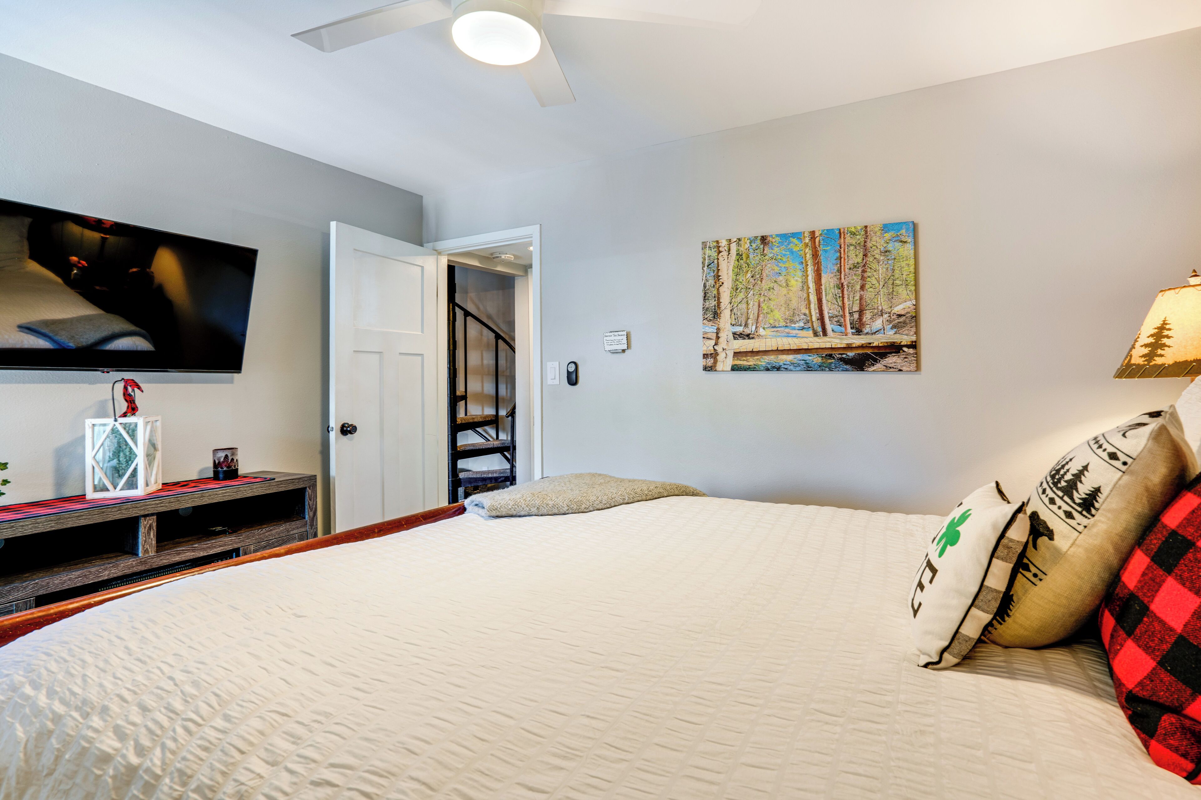 A bedroom with a bed, a TV mounted on the wall, a painting, and a lamp.