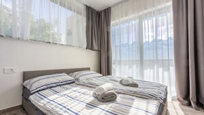 A hotel room with a large bed, two pillows, a bedside table, and a window with curtains. - Modern vacation home with whirlpool surrounded by greenery (Crikvenica)