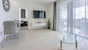 A modern living room with a flat-screen TV, a glass coffee table, a dining area with a chair, and a large window with curtains. - Modern vacation home with whirlpool surrounded by greenery (Crikvenica)