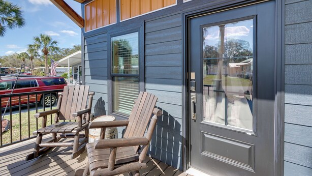 A wooden deck with Adirondack chairs, a covered patio, and a view of a red car and palm trees. - Rodeo Thrills & Backyard Bbqs! Lake Wales Retreat (River Ranch)