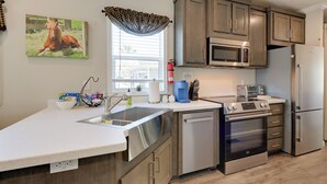 A modern kitchen with stainless steel appliances, wooden cabinets, and a large window with a view. - Rodeo Thrills & Backyard Bbqs! Lake Wales Retreat (River Ranch)