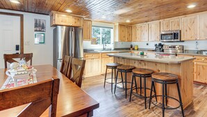 Cucina con mobili in legno, frigorifero in acciaio inossidabile, forno a microonde e angolo bar con sgabelli.
