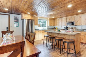 Una cocina con armarios de madera, un refrigerador de acero inoxidable, un microondas y una barra con taburetes.