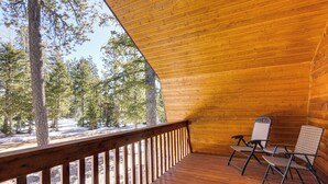 Un terrazzo in legno con ringhiera, due sedie e vista su una foresta.