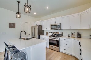 Une cuisine moderne avec des meubles blancs, des appareils en acier inoxydable et des luminaires suspendus.