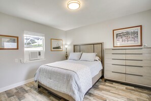 Quarto com cama, cómoda, janela e ar condicionado fixado na parede.