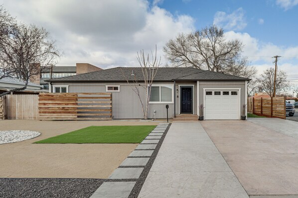 A modern two-story house with a garage, a front yard with a lawn and gravel path, and a wooden fence.