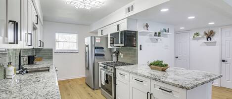 A modern kitchen with white cabinets, a granite countertop, stainless steel appliances, and a decorative ceiling light.