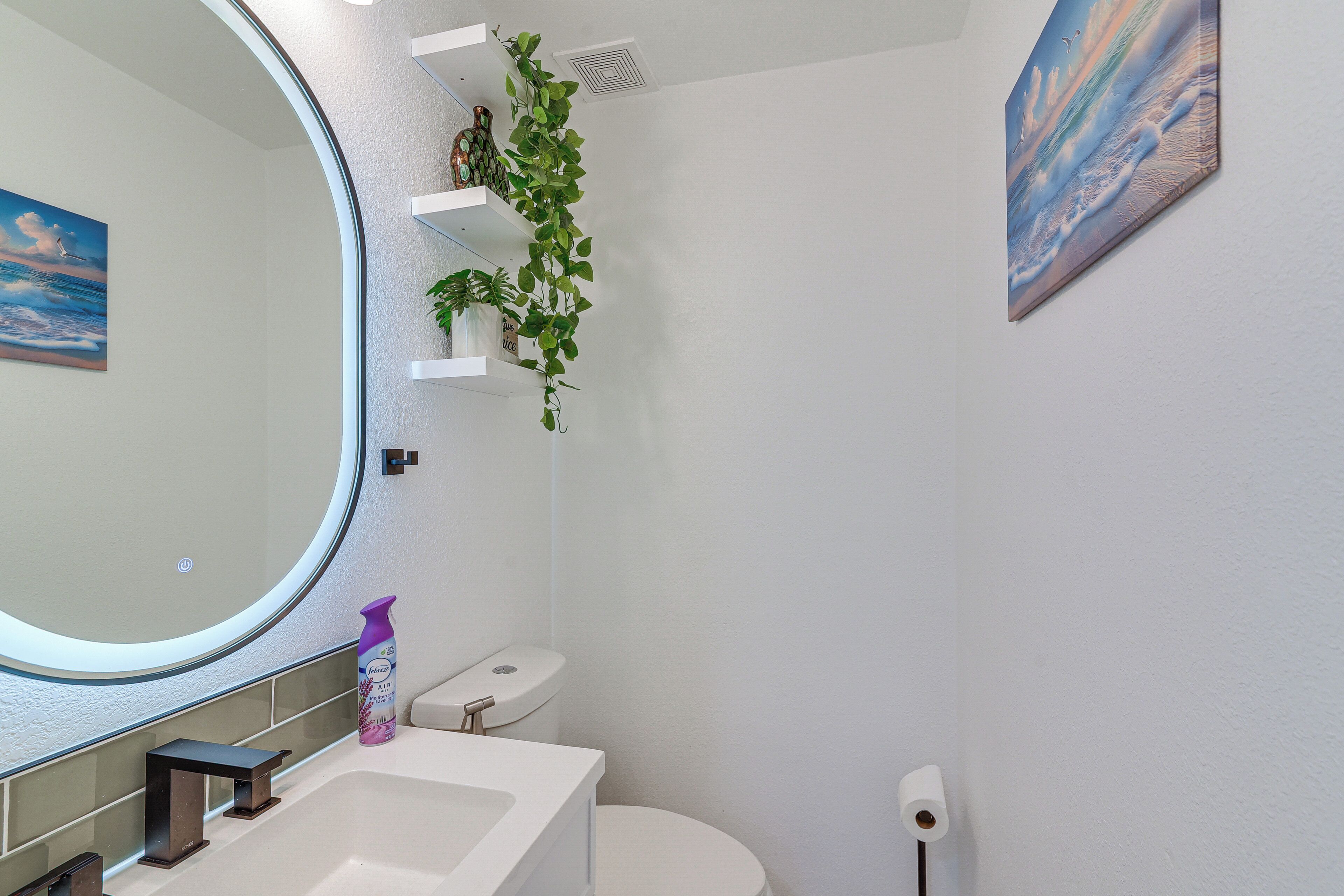 Un baño con inodoro, lavamanos, espejo y una planta en un estante.