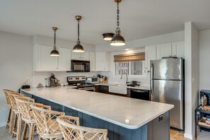A kitchen with white cabinets, a large island with bar stools, stainless steel appliances, and pendant lighting. - White Mtn Adventure Hub! Group Escape w/ Views (Bretton Woods)