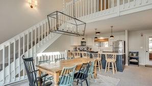 Uma sala de jantar espaçosa com uma mesa e cadeiras de madeira, uma cozinha com eletrodomésticos modernos e uma escadaria com corrimão branco.