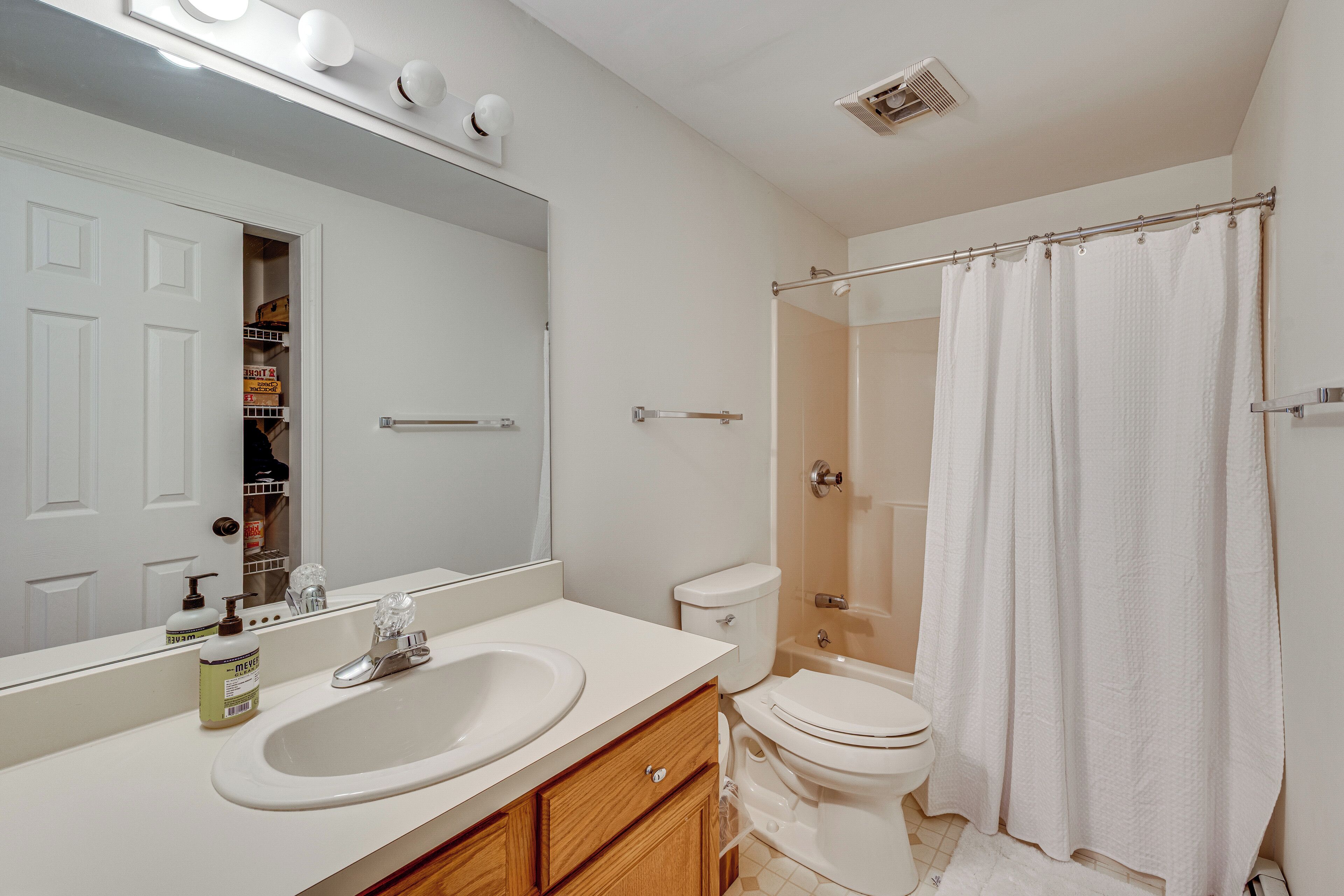 A bathroom with a white sink, mirror, toilet, and shower curtain.