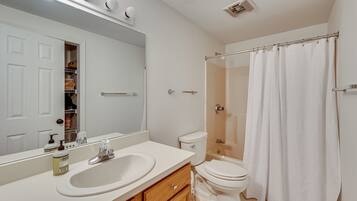 A bathroom with a white sink, mirror, toilet, and shower curtain.