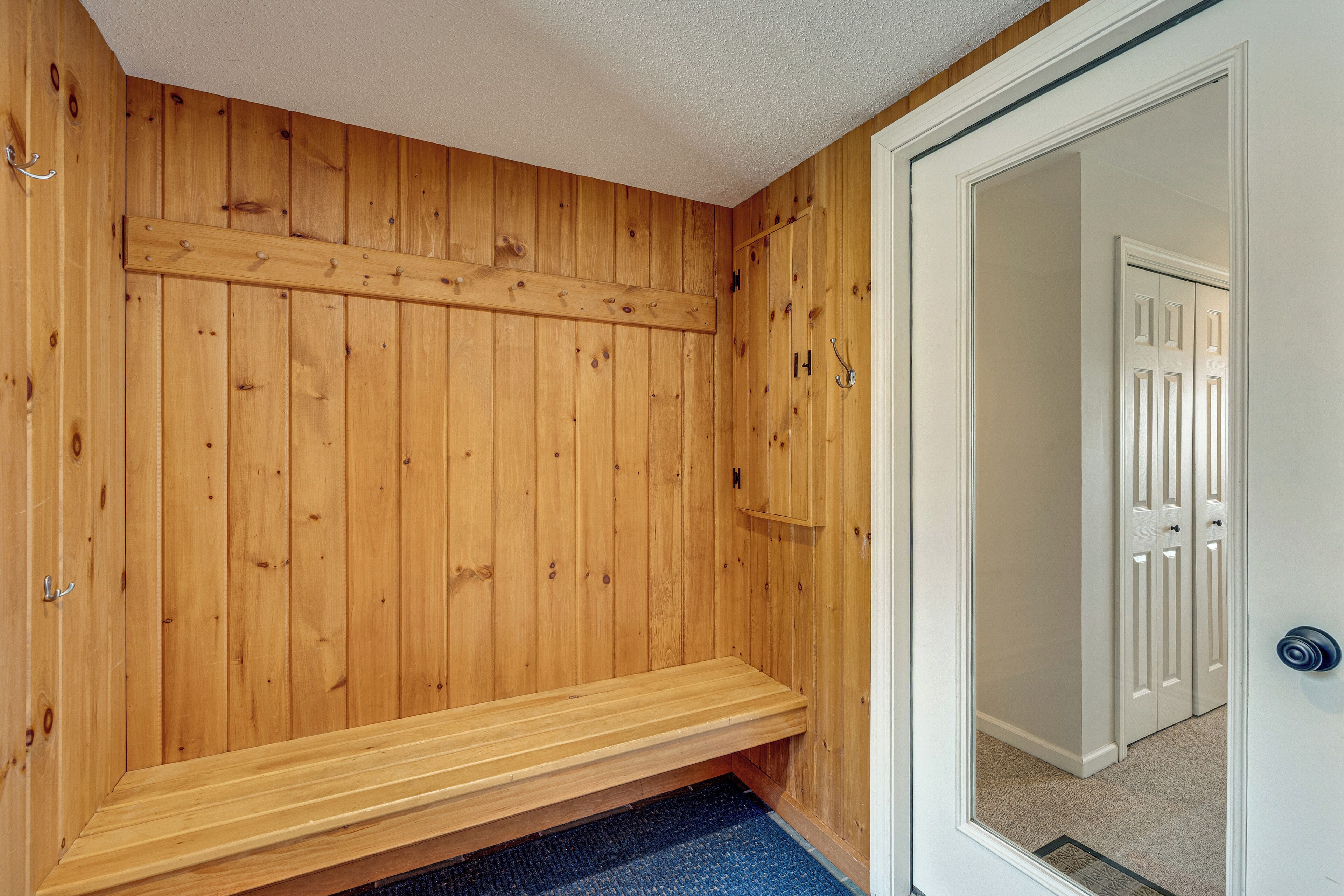 Ein Zimmer aus Holz mit einer Bank, einer Tür und einem Flur, der in einen anderen Raum führt.