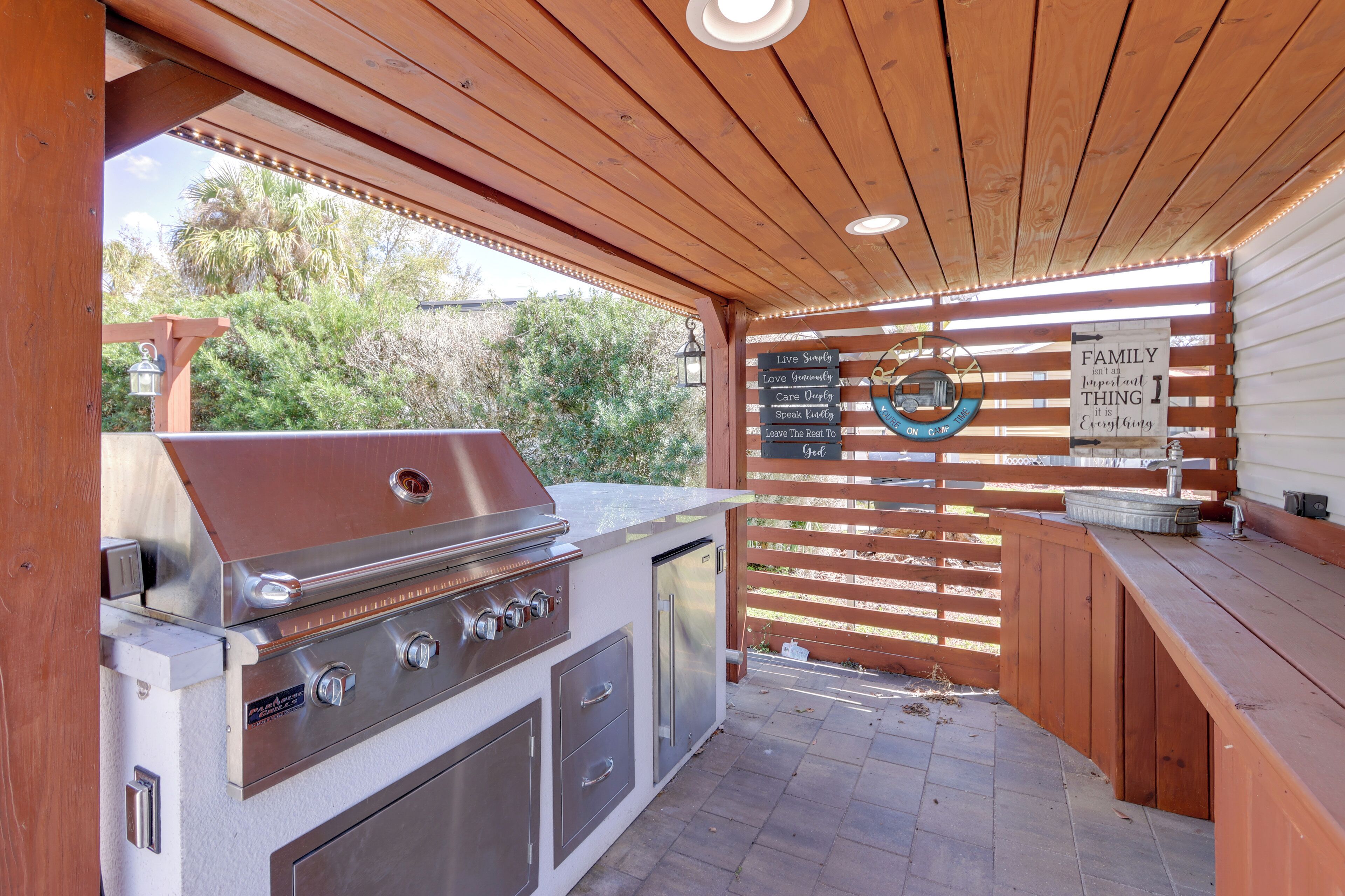 An outdoor kitchen with a grill, refrigerator, and wooden deck.