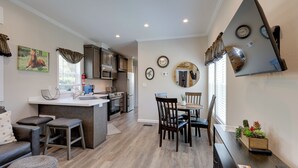 A modern kitchen with a central island, dining area with chairs, and a living space with a sofa and ottoman.