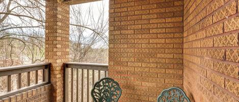 Une véranda couverte avec des murs en briques décorées, une balustrade en bois et deux fauteuils élégants.