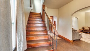 A wooden staircase with a metal railing, a living room with a sofa and a coffee table, and a window with curtains. - Ohio Valley Home Near Franciscan University! (Steubenville)