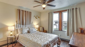 A bedroom with a bed, bedside lamps, a ceiling fan, a window with curtains, and a wooden nightstand. - Ohio Valley Home Near Franciscan University! (Steubenville)