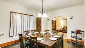 A dining room with a wooden table set for six, surrounded by chairs, a chandelier, and a kitchen area visible through an archway. - Ohio Valley Home Near Franciscan University! (Steubenville)