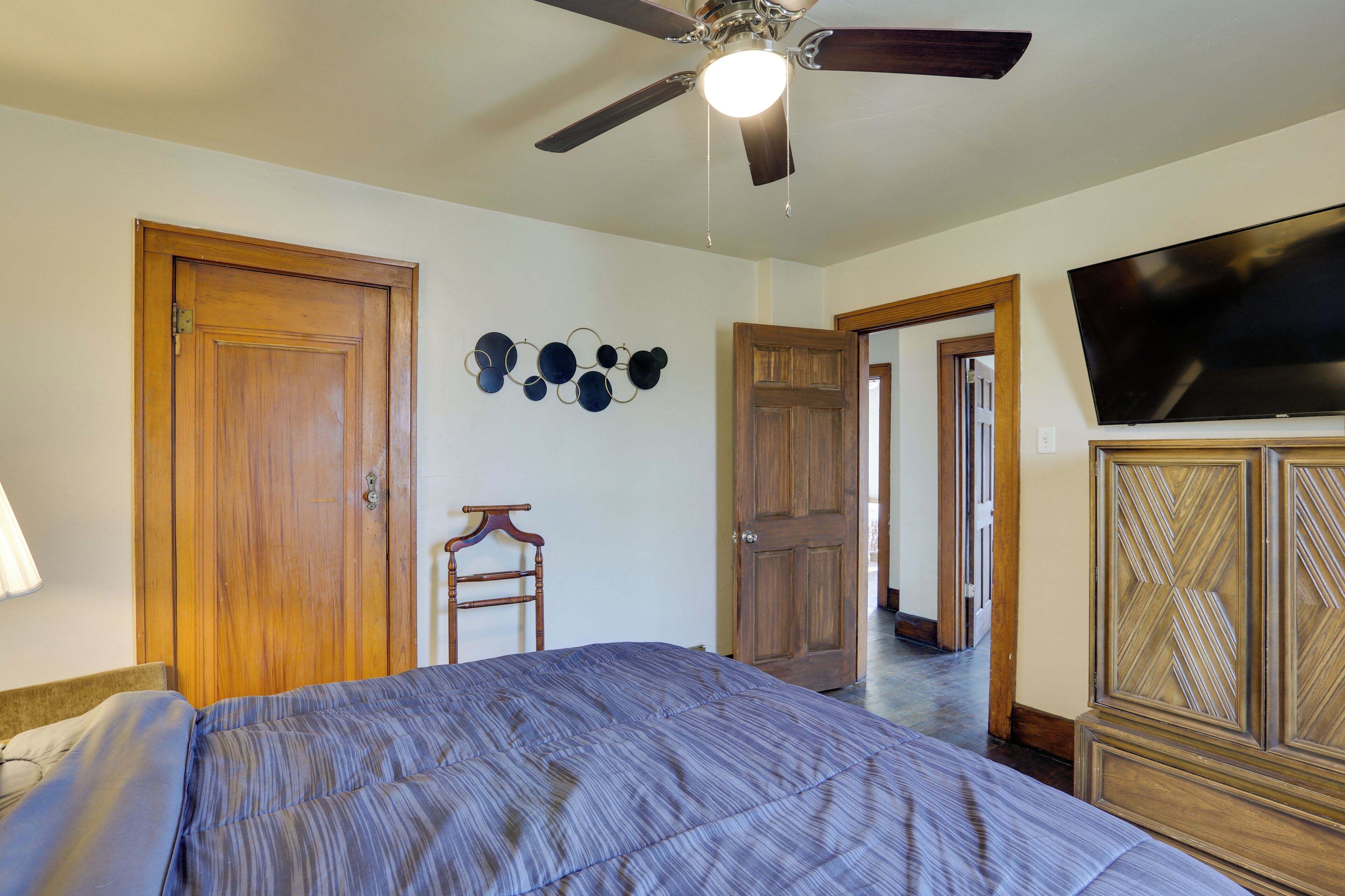 A bedroom with a bed, ceiling fan, wooden wardrobe, and a television.