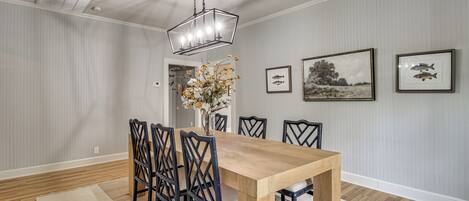 Un comedor con una mesa de madera, sillas negras, una araña y cuadros en la pared.
