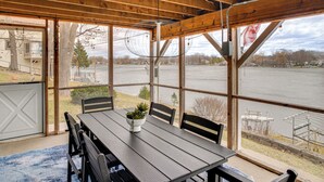 Un espacio de comedor al aire libre cubierto con mesa y sillas, ventanas amplias y vista a un cuerpo de agua.