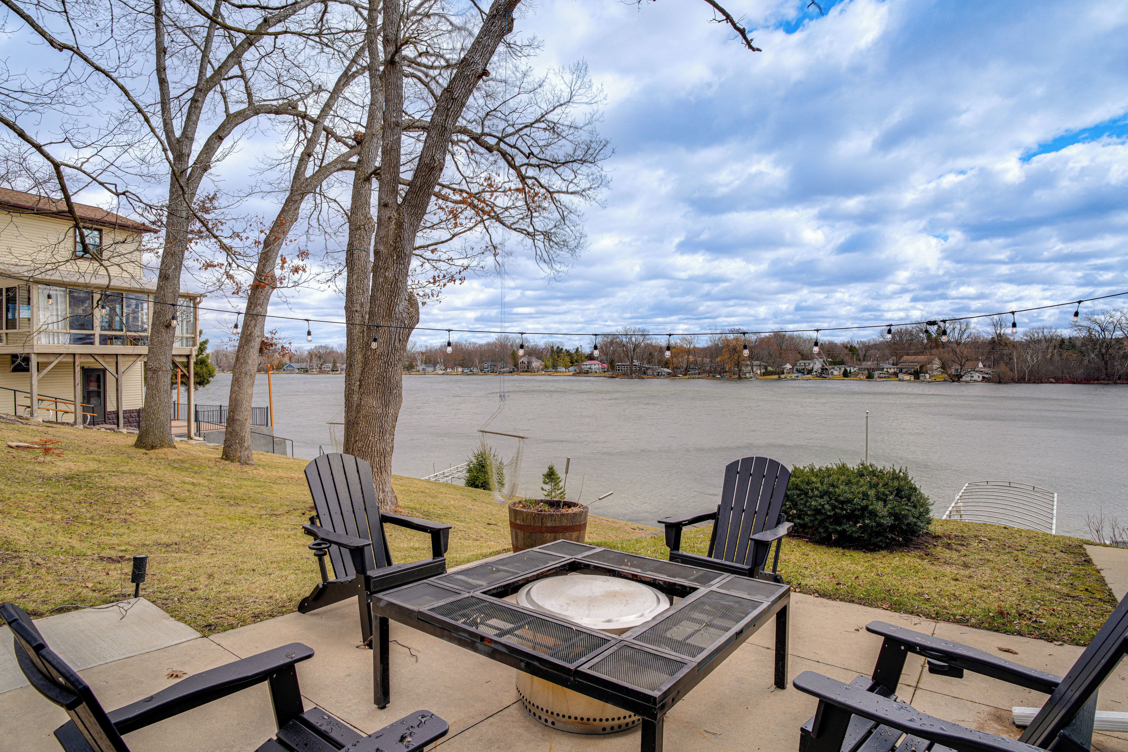 An outdoor seating area with a fire pit, four Adirondack chairs, and a view of a body of water.