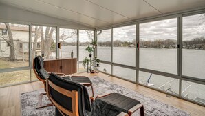 Una habitación moderna con ventanas amplias, una silla de madera, una mesita pequeña y una planta en maceta.