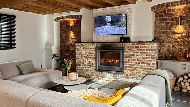 A living room with a stone fireplace, a television mounted above it, and a sofa. - Renovated, charming heritage farmhouse in the heart of the Flemish Ardennes (Oudenaarde)
