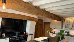 A kitchen with a black stove, white cabinets, and a wooden ceiling beam. - Renovated, charming heritage farmhouse in the heart of the Flemish Ardennes (Oudenaarde)