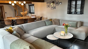 A modern living room with a sectional sofa, a dining area, and a staircase. - Renovated, charming heritage farmhouse in the heart of the Flemish Ardennes (Oudenaarde)