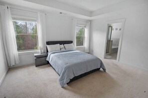 A bedroom with a bed, two windows, a nightstand, and a door leading to a bathroom. - Close to Airport/Private Patio/Full kitchen (Atlanta)
