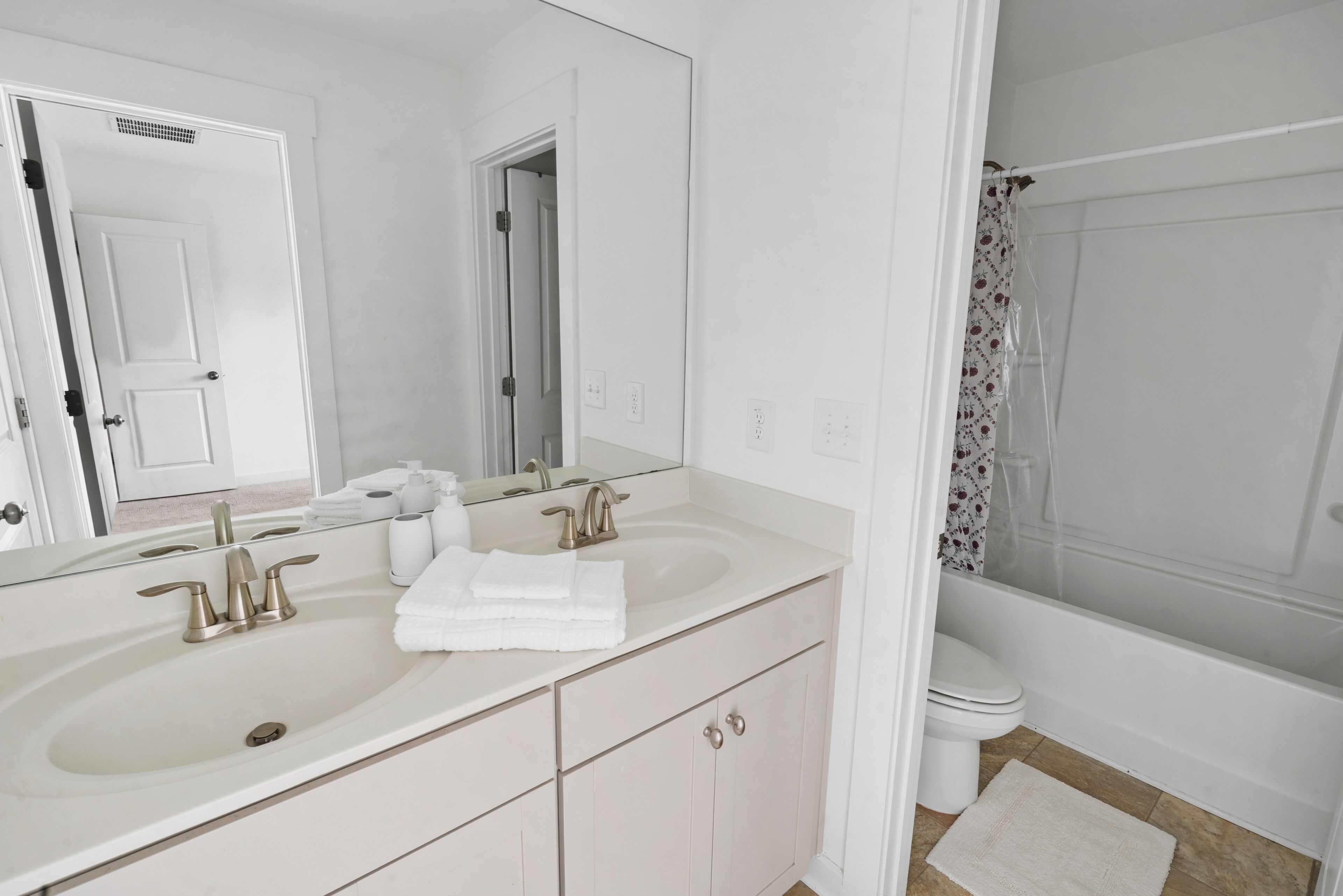 A bathroom with a double sink, a mirror, a toilet, and a shower.