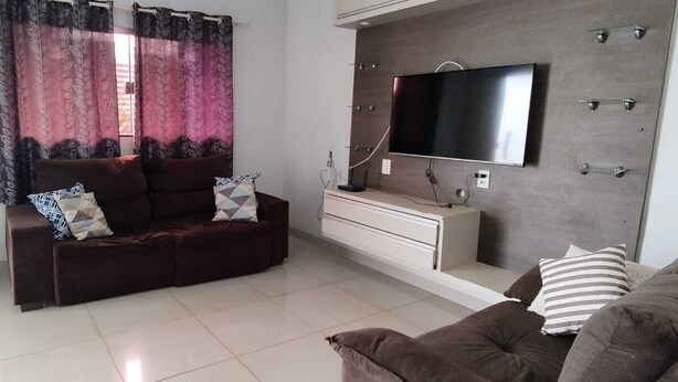 A living room with a sofa, a TV mounted on a wall, a small table, and a potted plant. - Each spacious exit leads to technoshow. (Rio Verde)