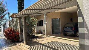 A covered parking area with a car, a building entrance, and a small garden with red flowers. - Each spacious exit leads to technoshow. (Rio Verde)