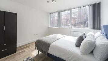 Een slaapkamer met een bed, een kledingkast, een raam met gordijnen en uitzicht op gebouwen.