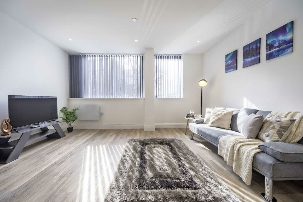 A modern living room with a flat-screen TV, a grey sofa, a patterned rug, and three framed pictures on the wall.