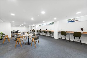 Ein moderner Arbeitsraum mit mehreren Tischen, Stühlen, einer Küchenzeile und Blick ins Freie.