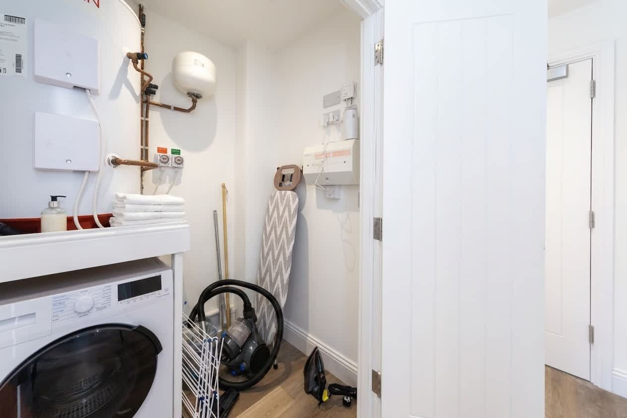 Een wasserette met een wasmachine, droger en een strijkplank.