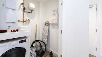 Een wasserette met een wasmachine, droger en een strijkplank.