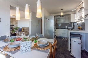 A modern kitchen with a dining area, featuring a refrigerator, cabinets, and a dining table set with plates, glasses, and a vase. - Modern apartment for 4 people with sea view (Crikvenica)