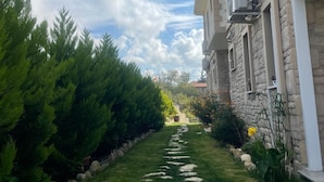 Un sentiero conduce a un edificio con muri in pietra e numerose finestre, immerso nel verde sotto un cielo sereno.