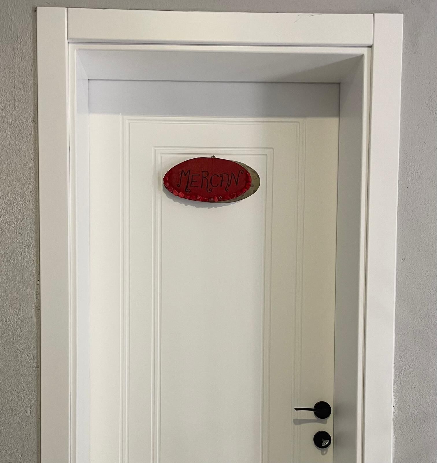 Una porta bianca con un cartello rosso che riporta la scritta 'MERCHANDISE' e una maniglia nera.