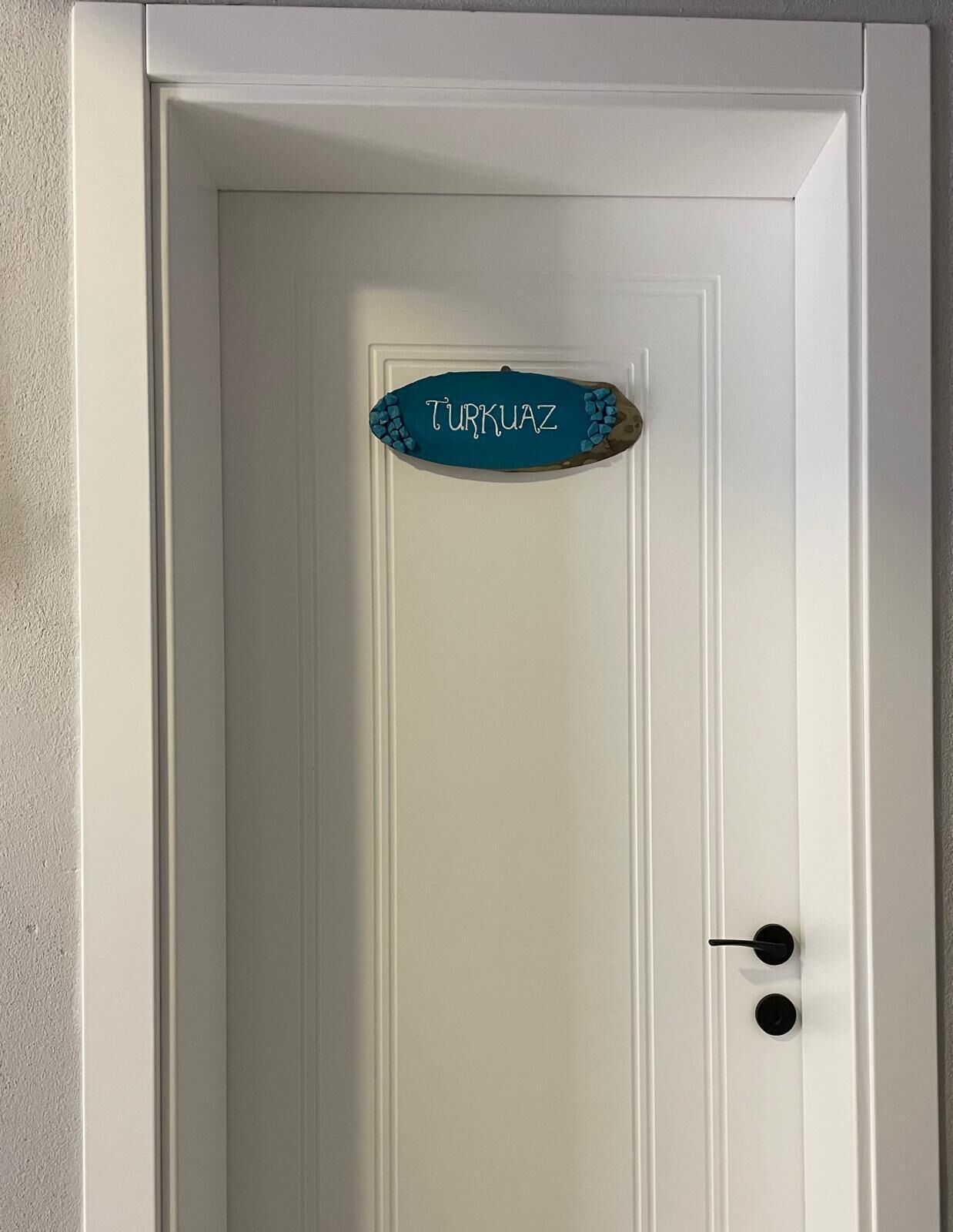 A white door with a sign that reads 'TURKUAZ' and a doorknob.