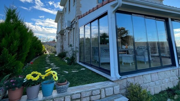 Una casa a due piani con un patio vetrato, gradini in pietra e piante in vaso.