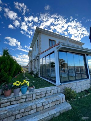 A two-story house with a glass-enclosed patio, stone steps, and potted plants. - Kyla Kocadere Pansiyon (Eceabat)
